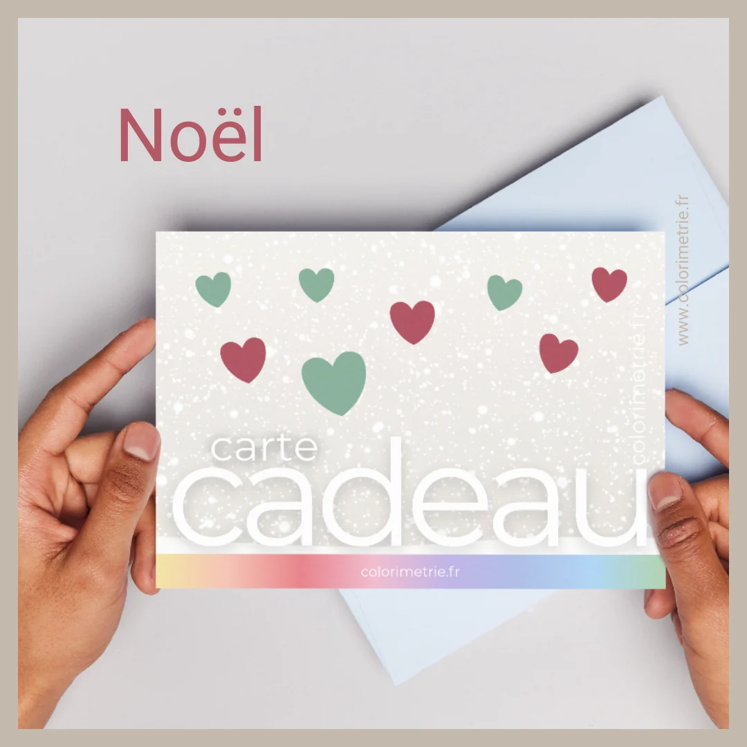Carte cadeau Ihana, édition Noël : une carte à fond neigeux ornée de cœurs rouges et verts, tenue entre deux mains devant une enveloppe bleue