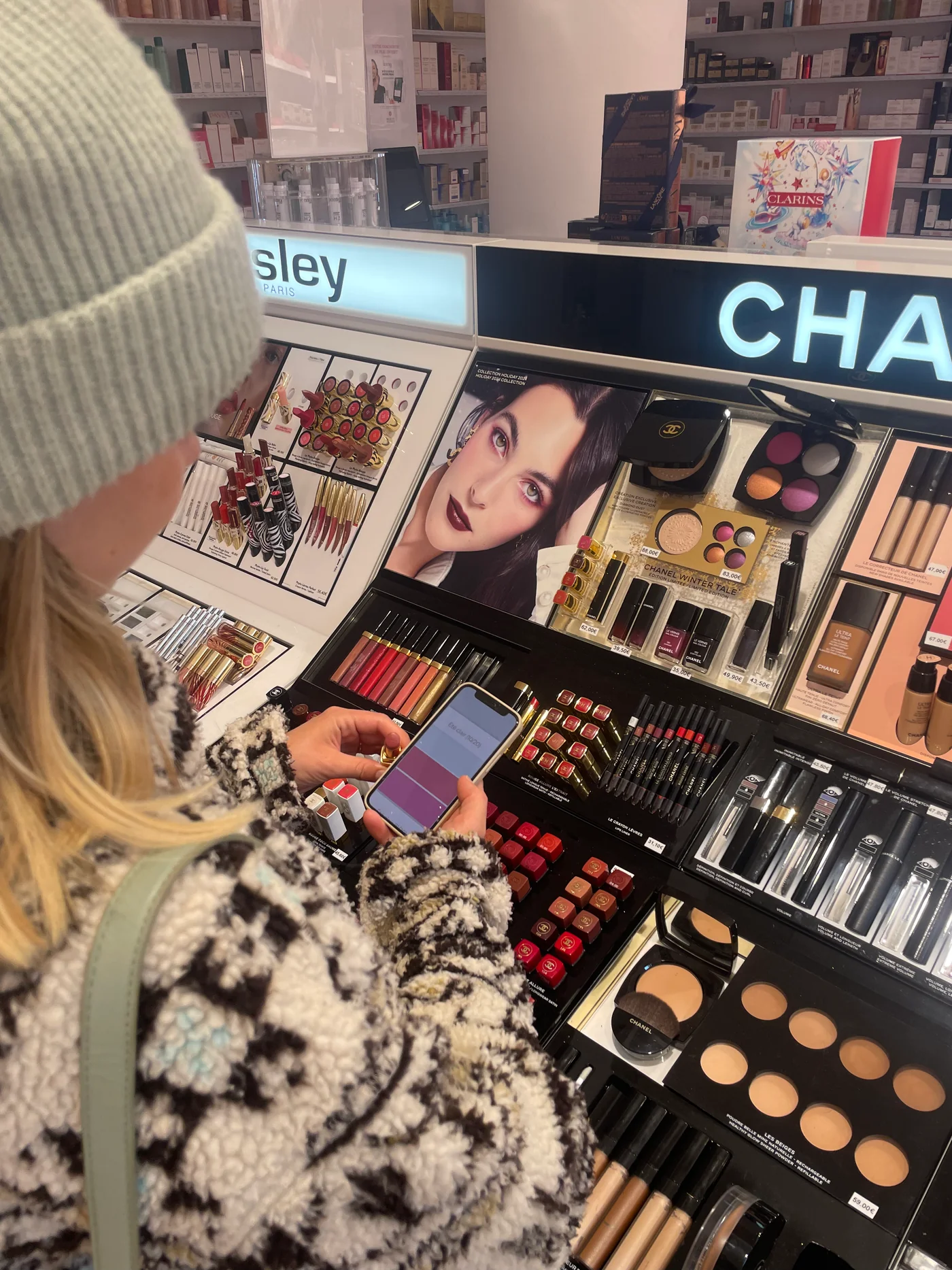 Une femme au rayon maquillage d’un magasin compare un produit à la palette digitale affichée sur son téléphone