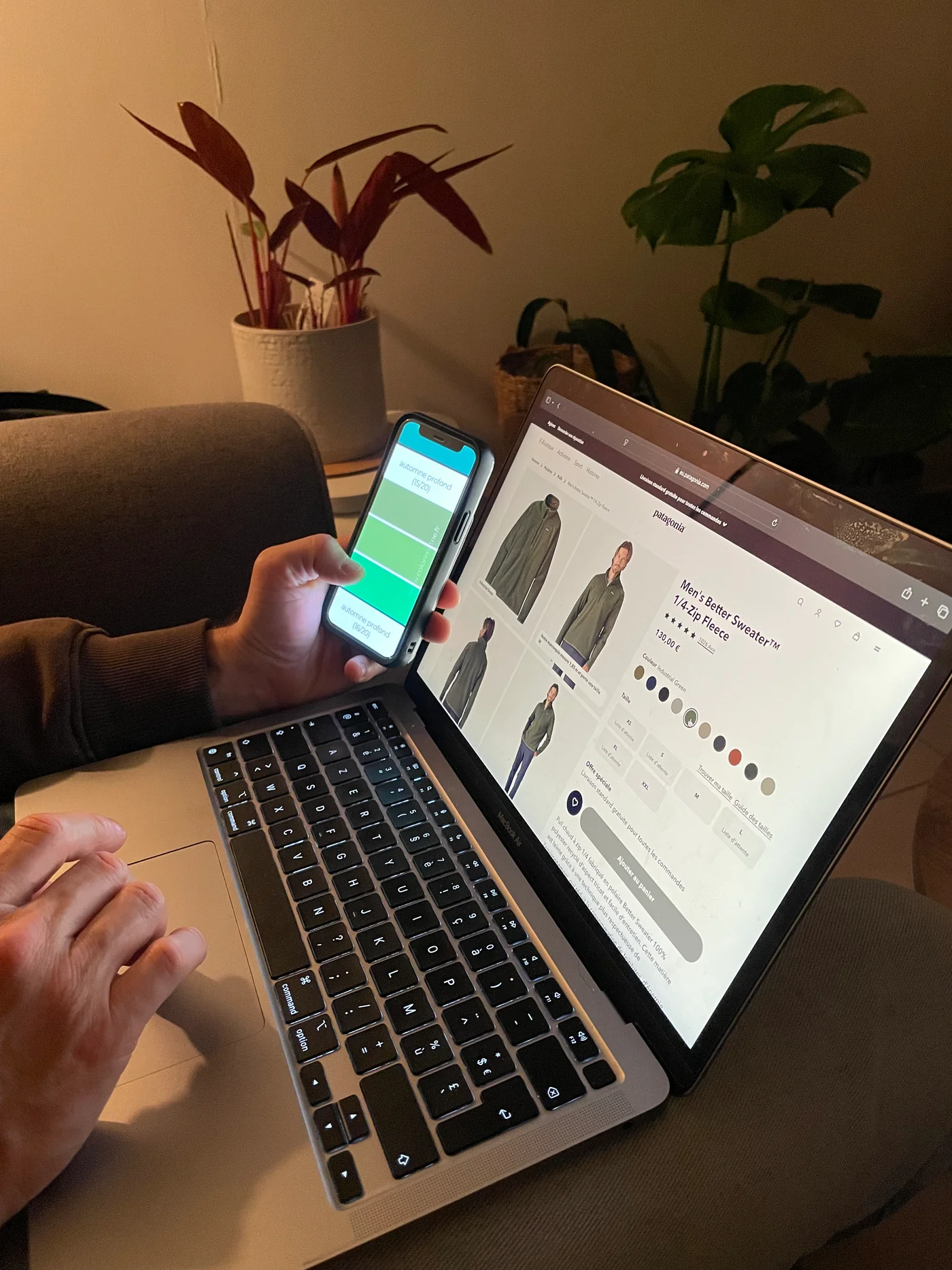 Une personne compare un pull à la palette digitale affichée sur son téléphone, devant la fiche du vêtement ouverte sur un ordinateur portable