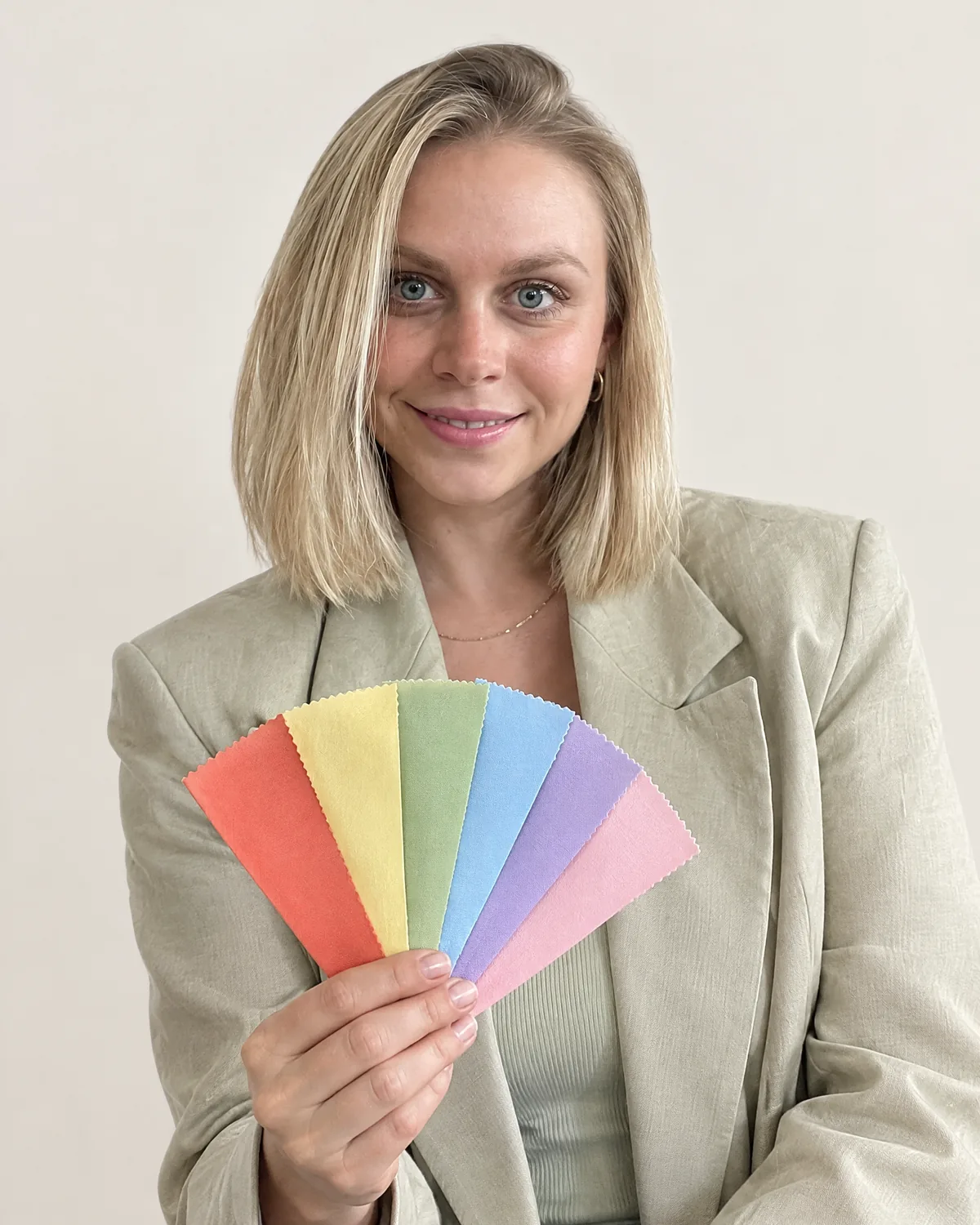 Lisa Routa souriante, face à l'objectif, présentant vers l'objectif un éventail d'étoffes de six couleurs : corail, jaune, vert, bleu, lilas et rose