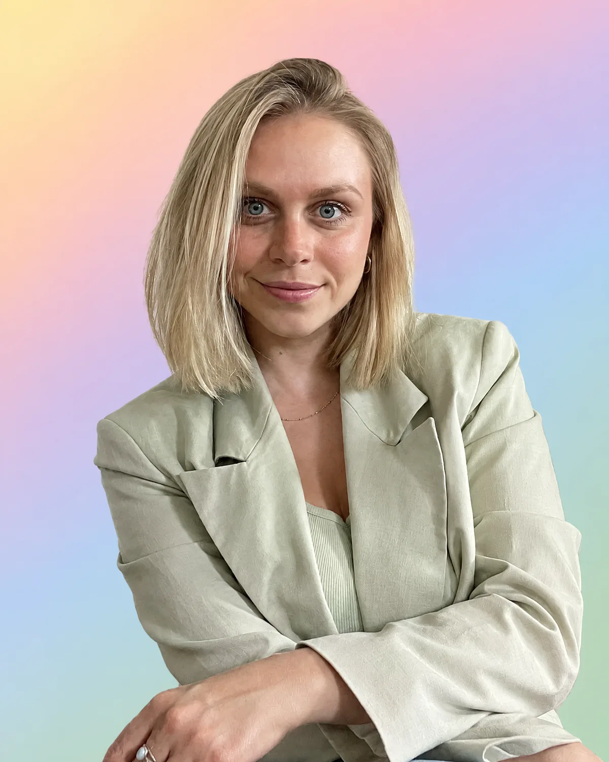 Lisa Routa, fondatrice d'Ihana Colorimétrie, en blazer de lin sauge, bras croisés, souriante, sur un dégradé pastel jaune, pêche, rose, lilas, bleu ciel et vert sauge