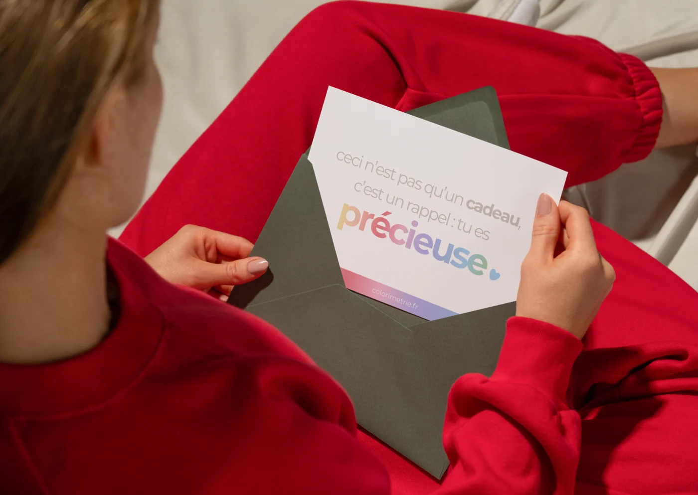 Une femme en pull rouge lit la carte « ceci n’est pas qu’un cadeau, c’est un rappel : tu es précieuse », sortie d’une enveloppe verte